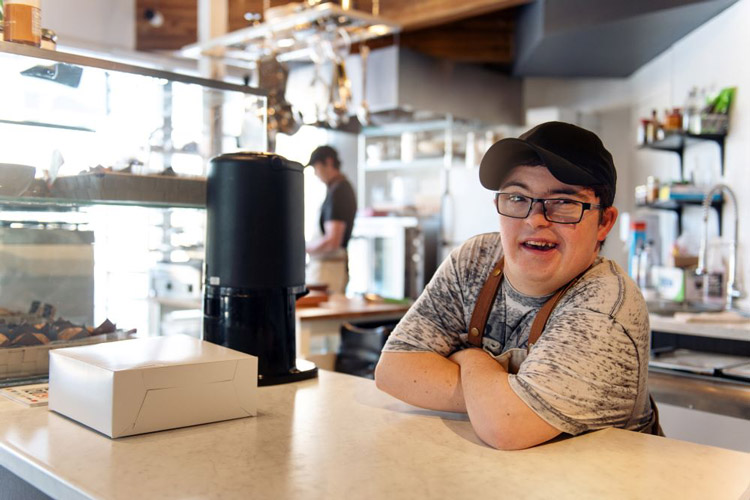 Man with a developmental disability smiling as he works behind the register at a coffee shop