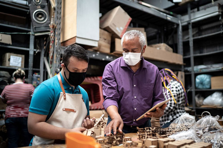 Two men wearing masks are working with metal in a workshop