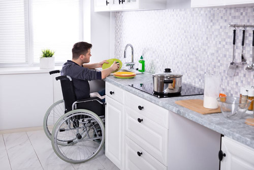 Man in wheelchair washing dishes in the kitchen sink