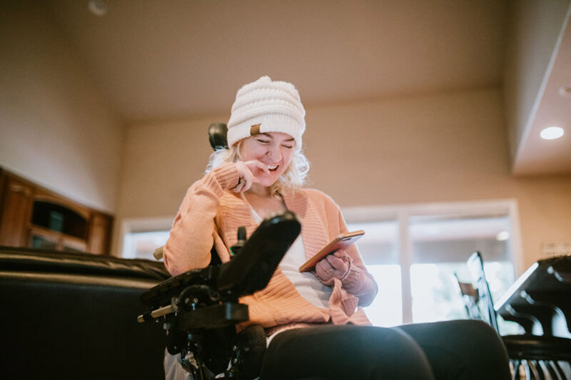Cheerful Woman In Wheelchair on Smartphone At Home