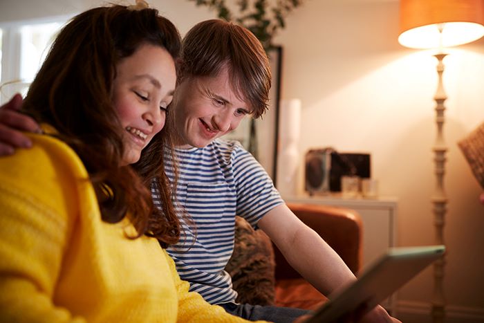 Man with a developmental disability laughing with a relative while looking on a tablet device.