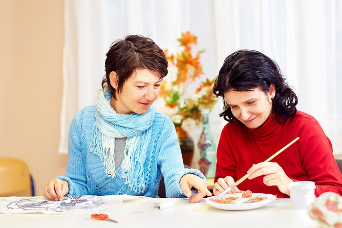 Two women with developmental disabilities painting with each other at a table.