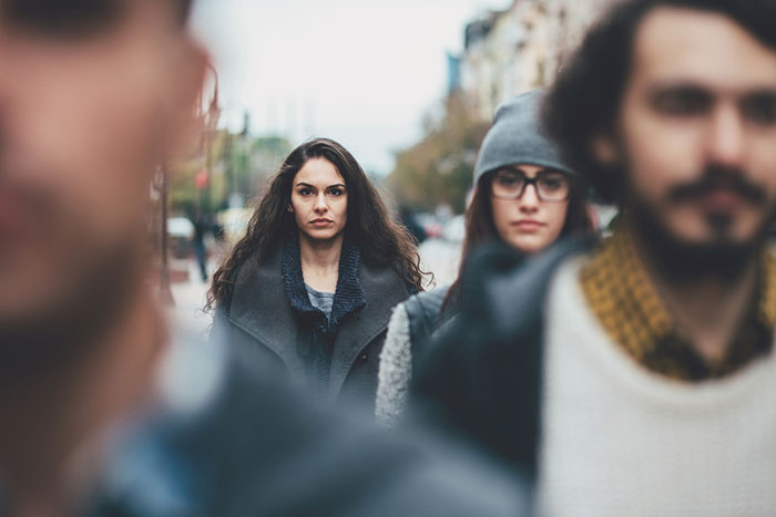 Portrait of a serious young woman among other defocused faces on the street