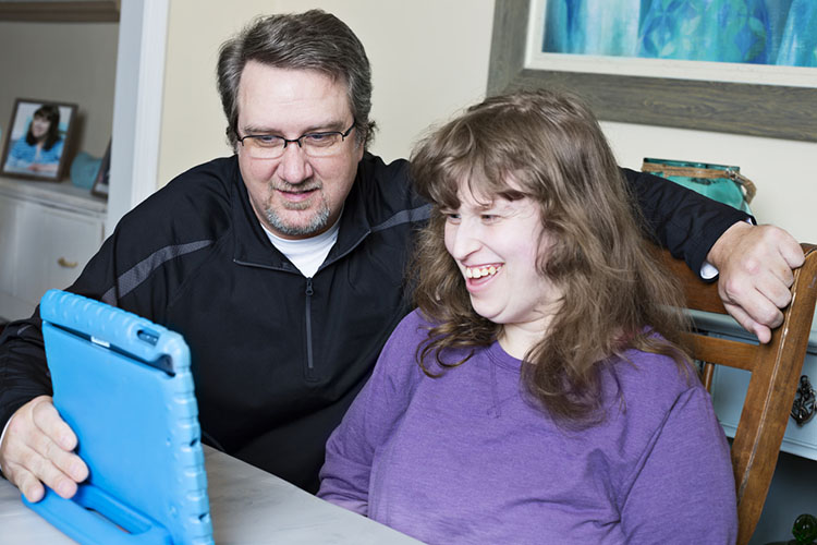Dad has to assist his intellectually disabled daughter during virtual school. They both smile at the digital tablet as the teacher communicates to both of them what today's lesson plan will be.