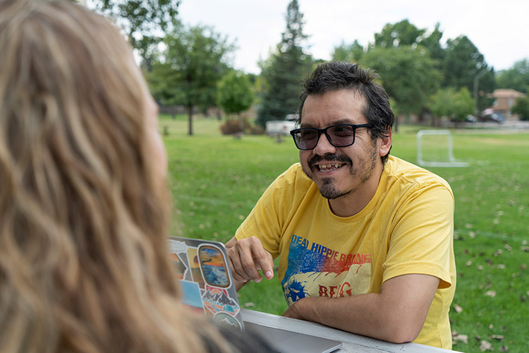 Man with a disability sitting at a picnic table outdoors looking at his laptop