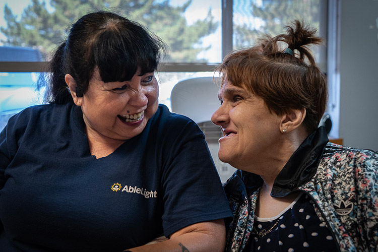 A female AbleLight employee and a woman with a developmental disability smiling together