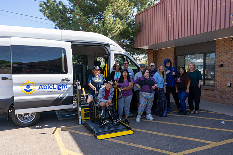 Group of AbleLight team members and people with developmental disabilities in front of an AbleLight van