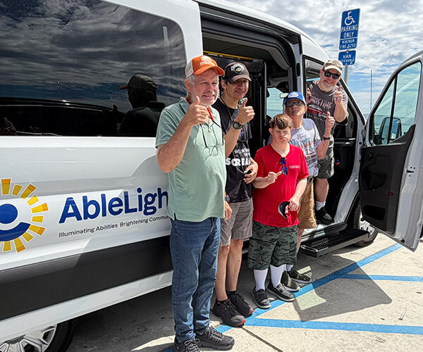 AbleLight team members and individuals supported in front of an AbleLight van