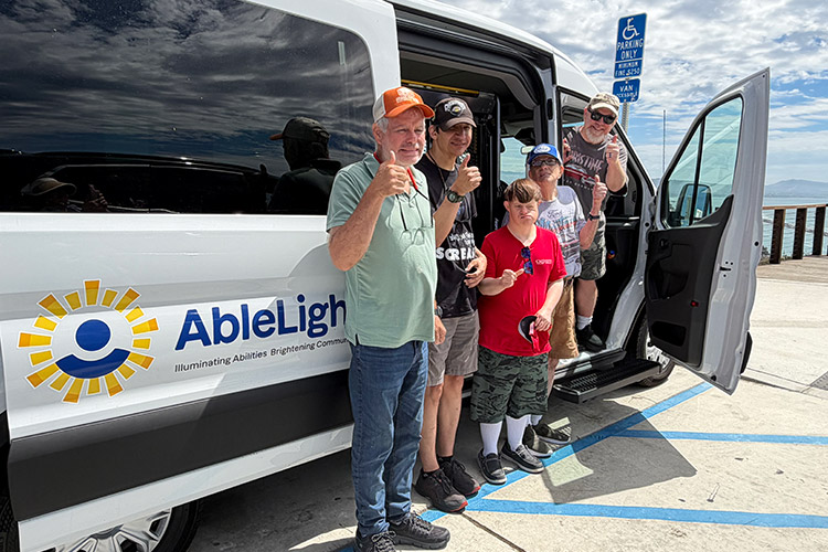 AbleLight team members and individuals supported in front of an AbleLight van
